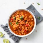 A vertical shot of chickpea curry chana masala with lime in a bowl on a white surf